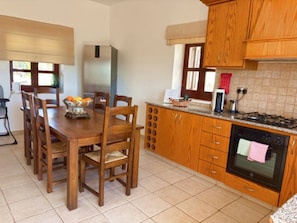 A kitchen with wooden cabinets, a dining table with chairs, a refrigerator, a stove, and a window with blinds.