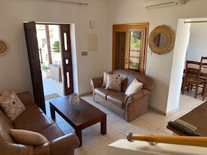 A living room with a brown leather sofa, a wooden coffee table, and a dining area with wooden chairs and a table.
