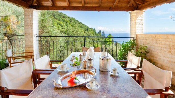 Una terrazza con un tavolo apparecchiato per la colazione, con vista su un paesaggio montuoso.