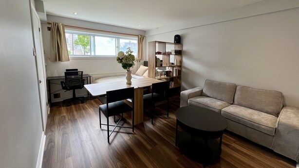 Un salon moderne avec un plancher en bois, un canapé, une table à manger avec des chaises, une petite table ronde et une bibliothèque.
