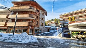 Una strada innevata con edifici in legno, un cartello per un ristorante e vista su una montagna.