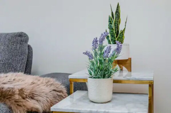 Un petit pot blanc, à la texture particulière, contenant des plantes vertes et violettes, posé sur une table dont le dessus est en marbre.