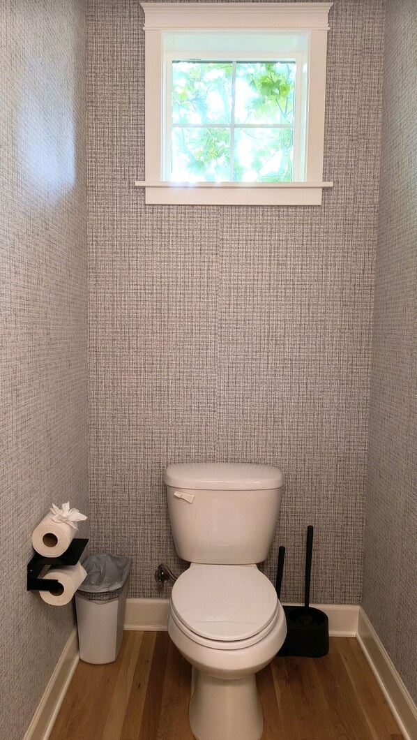 A small bathroom with a toilet, a window, and a trash can. - Modern Edmonds Escape: Spacious, 3BDRM, Fireplace (Edmonds)