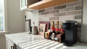 A kitchen with a coffee maker, a kettle, a coffee machine, a book titled "Women & Nature", and a coffee dispenser.