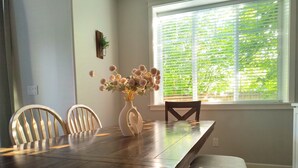 A dining table with chairs, a vase with flowers, and a window with blinds.