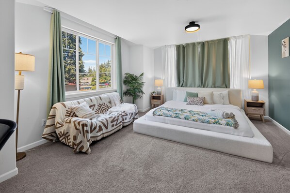 A bedroom with a bed, a sofa, two bedside tables, a lamp, and a window with curtains. - Modern Edmonds Escape: Spacious, 3BDRM, Fireplace (Edmonds)