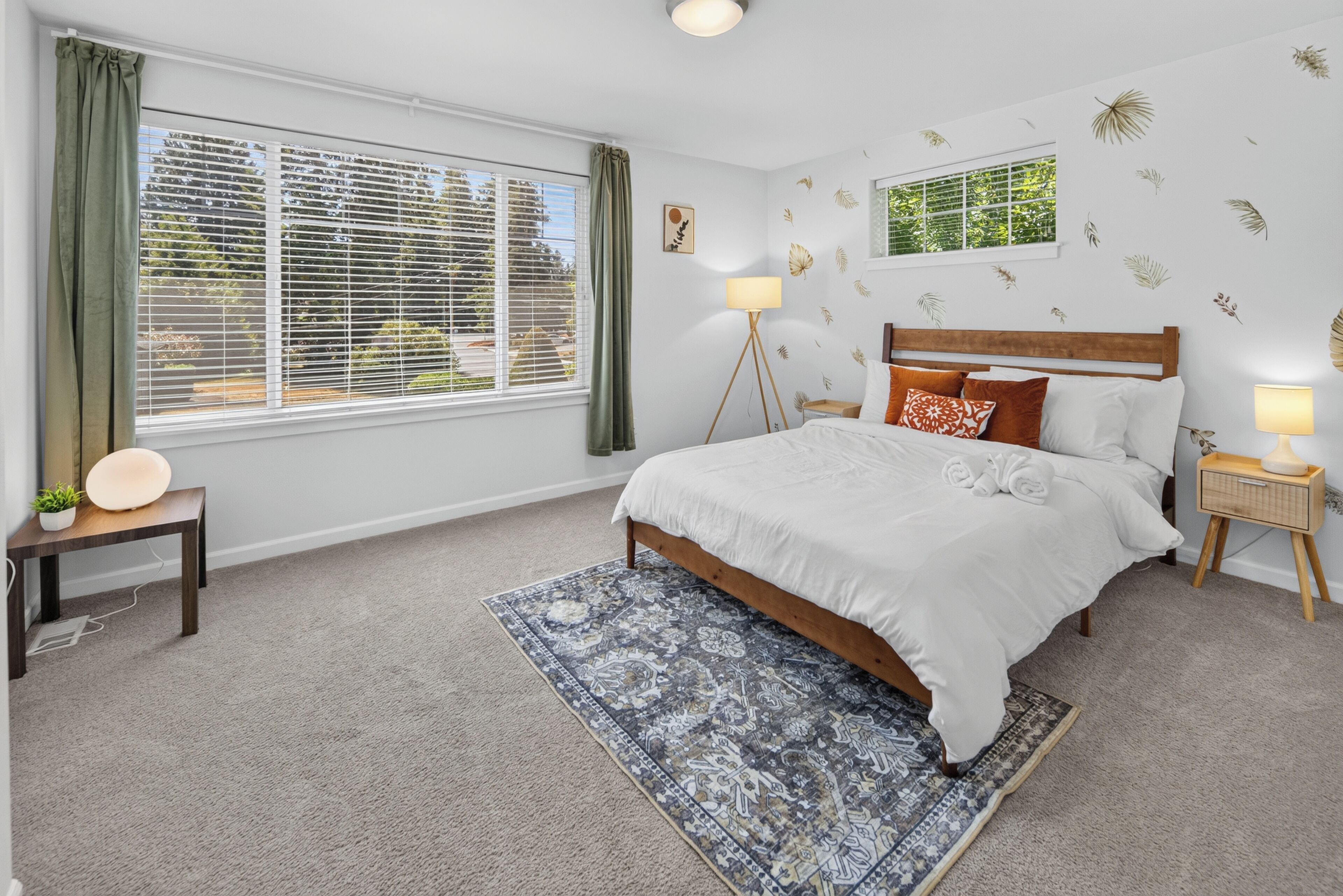 A bedroom with a large bed, two bedside lamps, a floor lamp, a window with blinds, and a patterned rug.