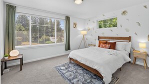 A bedroom with a large bed, two bedside lamps, a floor lamp, a window with blinds, and a patterned rug.
