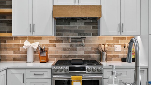 A modern kitchen with white cabinets, a brick backsplash, a gas stove, and a stainless steel sink.