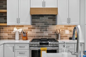 A modern kitchen with white cabinets, a brick backsplash, a gas stove, and a stainless steel sink. - Modern Edmonds Escape: Spacious, 3BDRM, Fireplace (Edmonds)