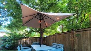 An outdoor patio with a table and chairs, a large umbrella, and a wooden fence.