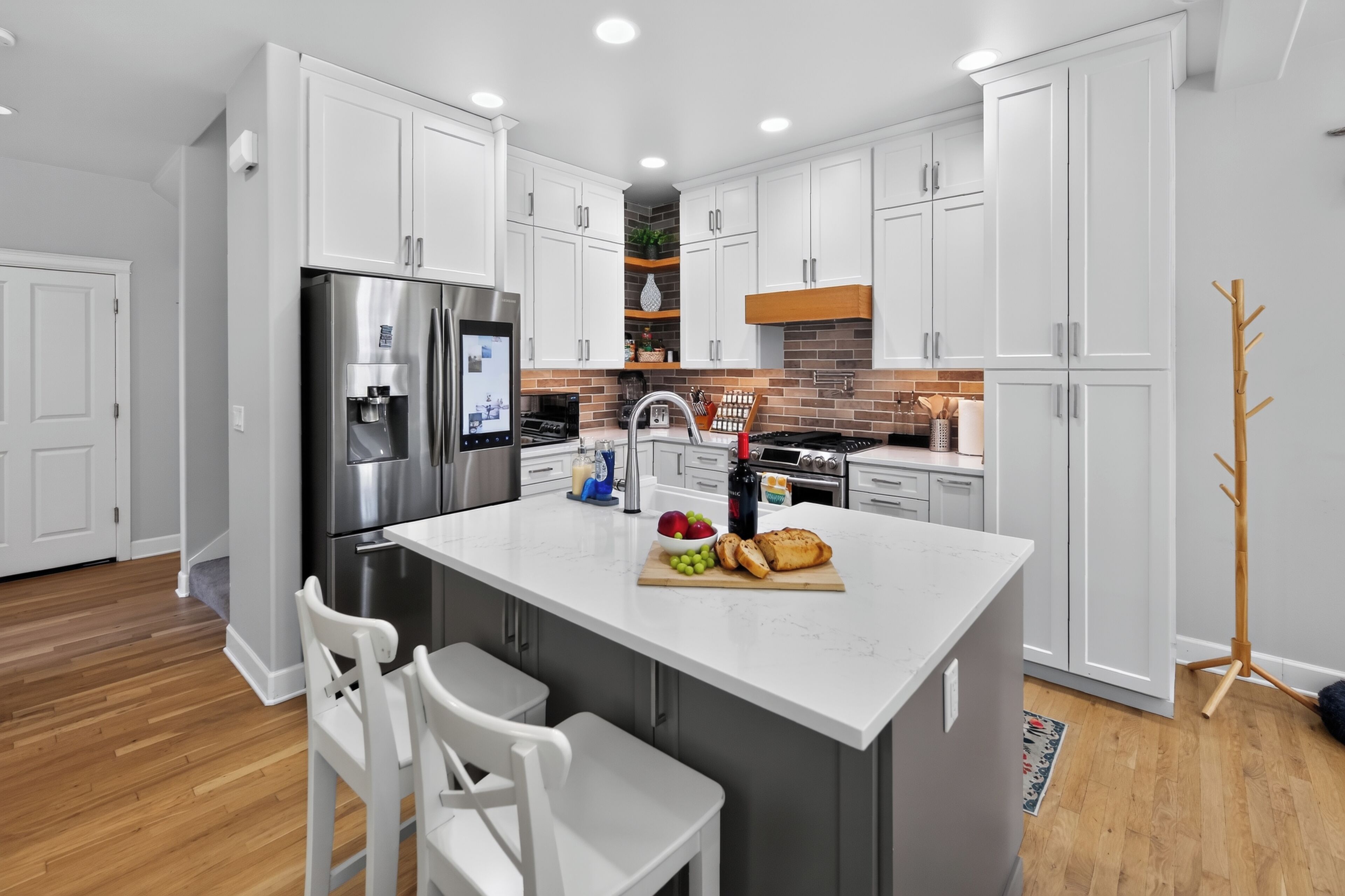 A modern kitchen with white cabinetry, stainless steel appliances, and a central island with seating.