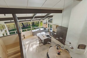 A modern kitchen with a central island, a dining area with a round table, and large windows offering a view of greenery. - The Sawtooth Modern | Designer Build | Hot Tub | River Access (Ketchum)