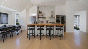 Een moderne keuken met een centraal eiland, barkrukken en een eethoek met een lange tafel en stoelen.