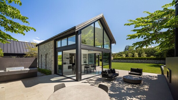 Een modern huis met een glazen patio, buitenmeubels en een stenen muur.