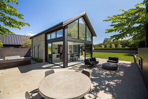 Una casa moderna con un patio de cristal, mobiliario exterior y un muro de piedra.