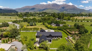 A large, modern house with a spacious yard, surrounded by lush greenery and mountains in the background. - Arrowtown Luxury Estate - NEW SPA and use of pool, tennis courts and gym (Arrowtown)