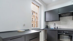 Una cocina moderna con armarios oscuros, horno integrado y ventana con vista a un edificio.