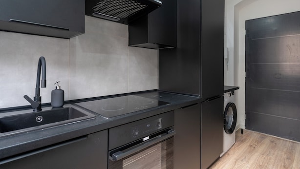 Una cocina moderna con lavavajillas integrado, un lavabo con grifo y un horno negro.