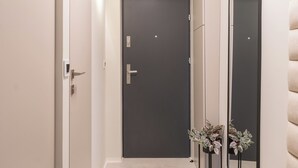 Un pasillo con una puerta oscura, un espejo y una planta.