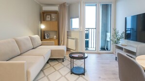 Una sala moderna con sofá, una mesita, televisor y un balcón con vistas.