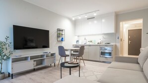Una sala moderna con televisor de pantalla plana, un sofá, una zona de comedor con sillas y una cocina con armarios y electrodomésticos.