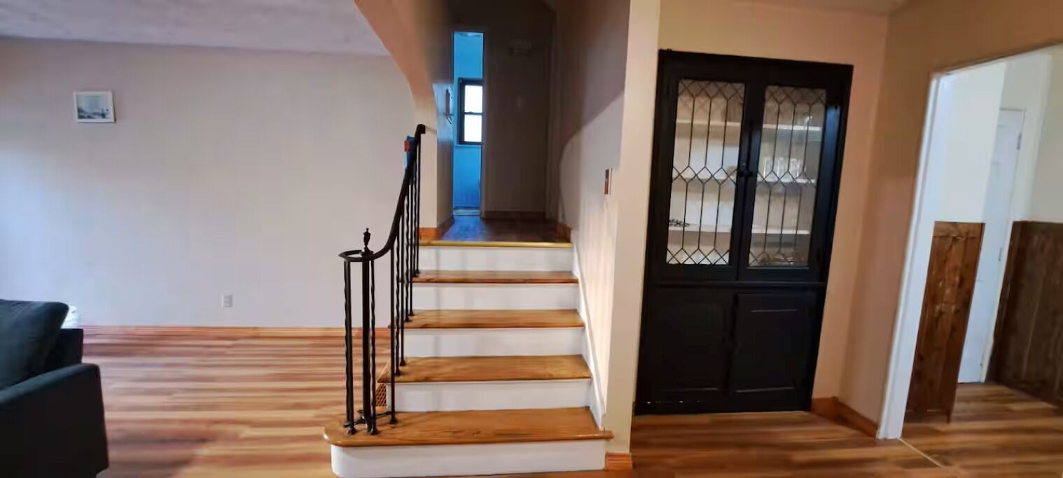 Un escalier avec des marches en bois et des rampes noires, menant à une porte surmontée d’un portail en métal.