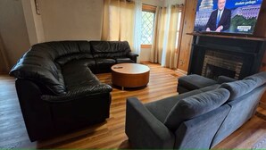 Ein Wohnzimmer mit einem schwarzen Ledersofa, einem runden Couchtisch und einem grauen Sofa. Ein Fernseher ist über einem Kamin angebracht.