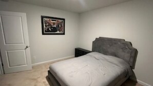 A bedroom with a bed, a door, a framed picture on the wall, and a nightstand. - Masters 2026 Rental Home w/Additional Loft in Grovetown, GA! (Grovetown)