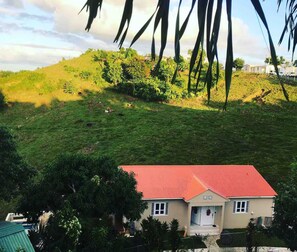 A house with a red roof, surrounded by lush greenery and a hilly landscape. - Apartments Pepe's View - C (Aguada)