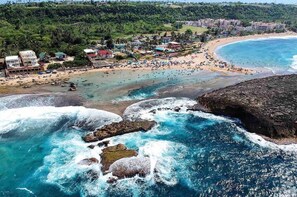 A coastal area with a beach, rocky shoreline, and buildings in the background. - Apartments Pepe's View - C (Aguada)