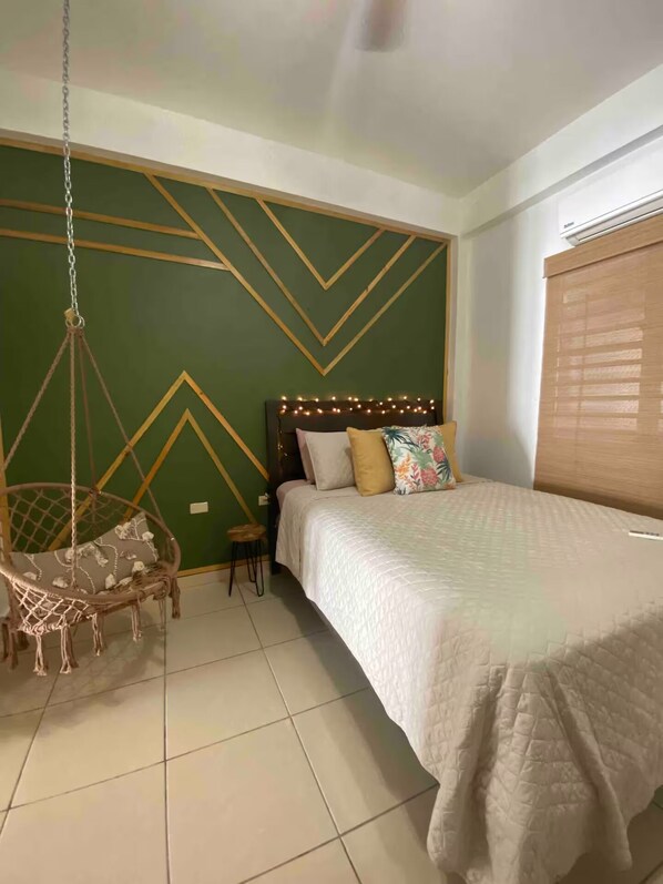 Ein Schlafzimmer mit einem Bett, einem Hängesessel und einem geometrischen Wandmuster.