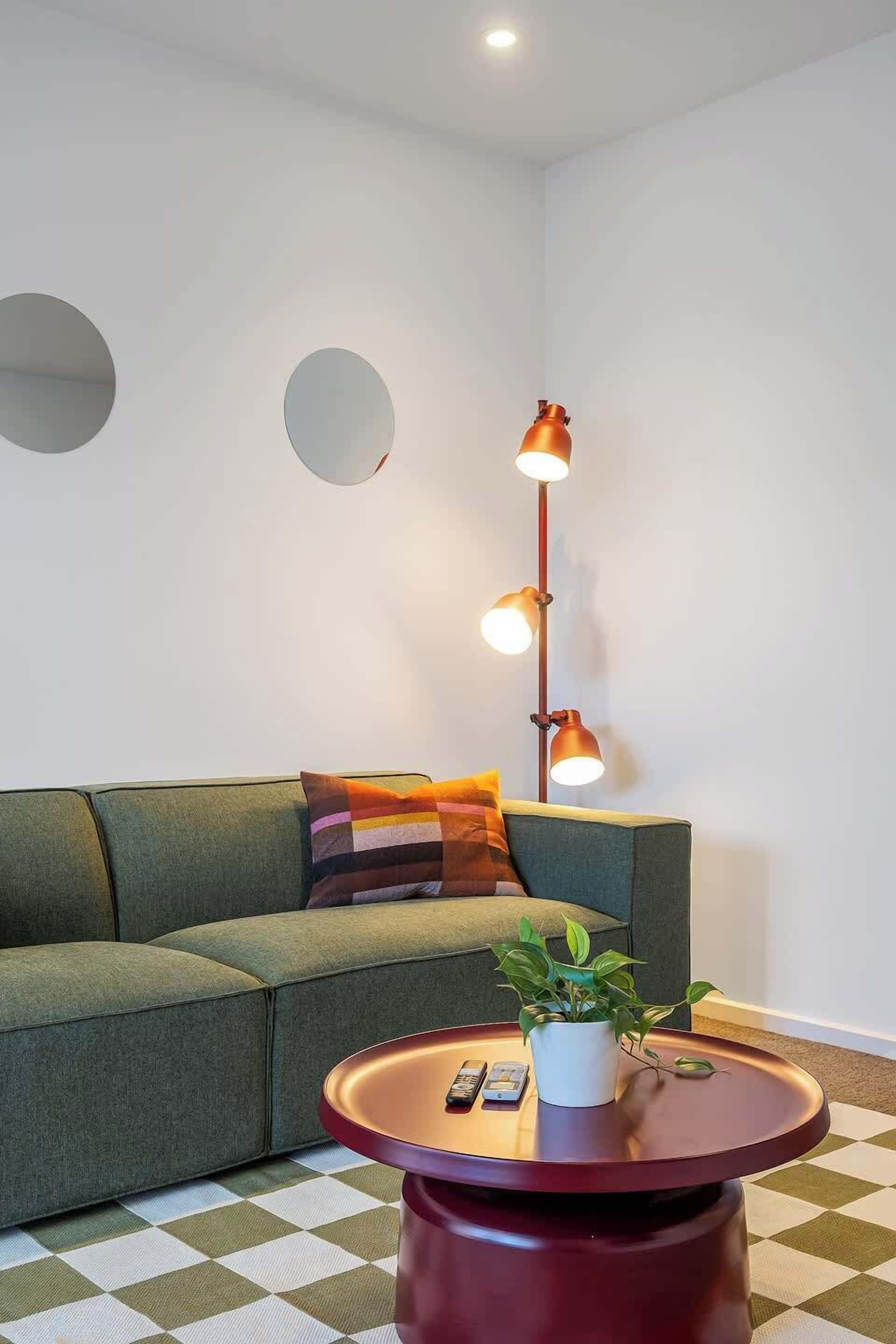 Ein modernes Wohnzimmer mit einem grünen Sofa, einem runden roten Tisch mit einer Pflanze und einer Stehlampe.