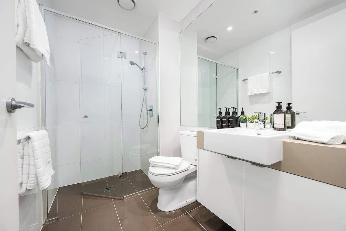 A modern bathroom with a glass-enclosed shower, a white toilet, and a vanity with a mirror.