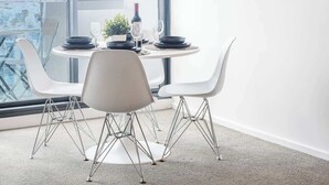 Un espace de restauration moderne avec une table ronde, des chaises blanches et une vue sur la ville grâce à de grandes fenêtres.