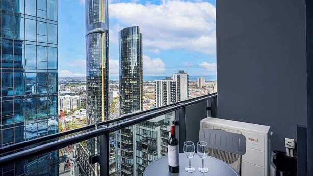 Un balcon avec une table, une bouteille de vin et des verres, donnant sur un paysage urbain avec de modernes gratte-ciel.
