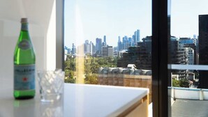 En vandflaske og et glas på et bord med udsigt til byens skyline gennem et vindue.