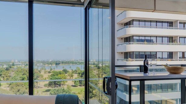 En moderne lejlighed med balkon, et glasbord og udsigt til sø og grønne områder.