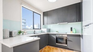 Et moderne køkken med mørke skabe, en hvid bordplade, indbygget ovn og et vindue, der giver naturligt lys.