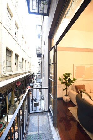 Une rue étroite en milieu urbain, avec un bar sur la gauche et un espace intérieur moderne, comprenant un canapé et une plante, sur la droite.