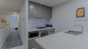 Une cuisine moderne avec des meubles gris, un plan de travail blanc, un évier, un four à micro-ondes et une cuisinière.