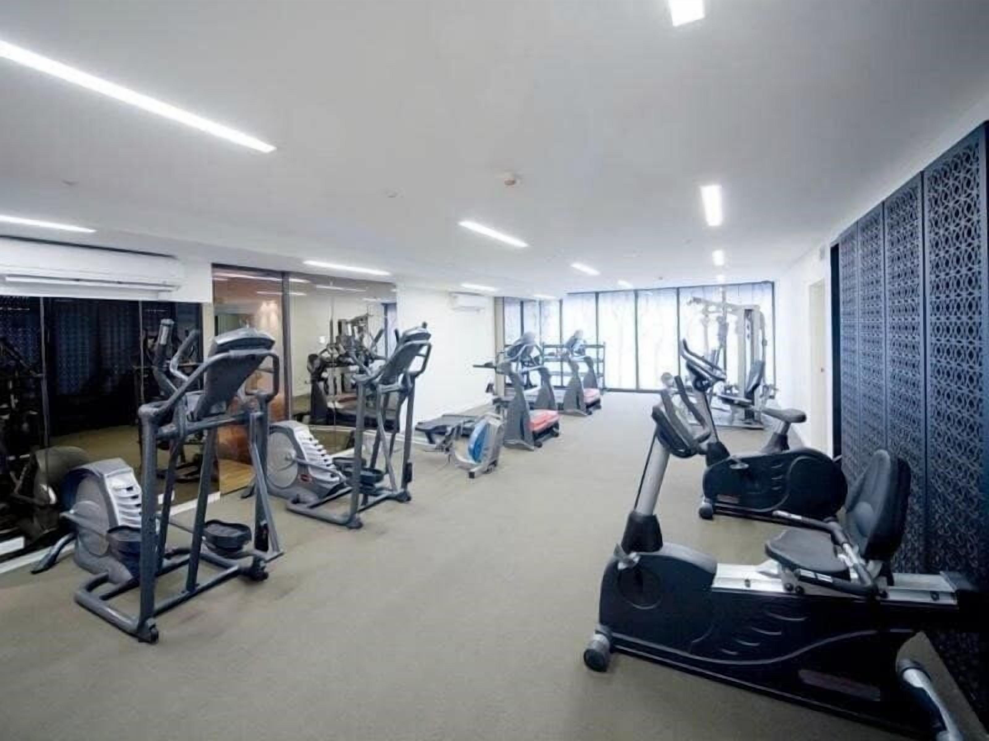 A gym with various cardio and strength training equipment, a large mirror, and a patterned wall.