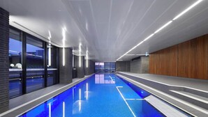 A modern indoor swimming pool with clear blue water, surrounded by glass walls and wooden paneling. - Scandinavian Suite, Lap Pool, Big Gym, Melbourne (South Yarra)