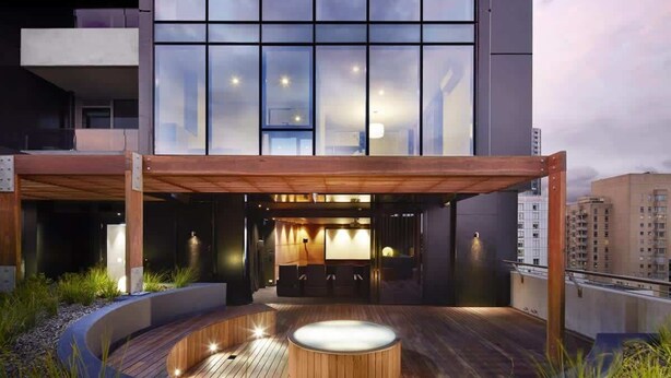 A modern building with a large glass facade, a wooden deck with a hot tub, and a covered seating area. - Scandinavian Suite, Lap Pool, Big Gym, Melbourne (South Yarra)