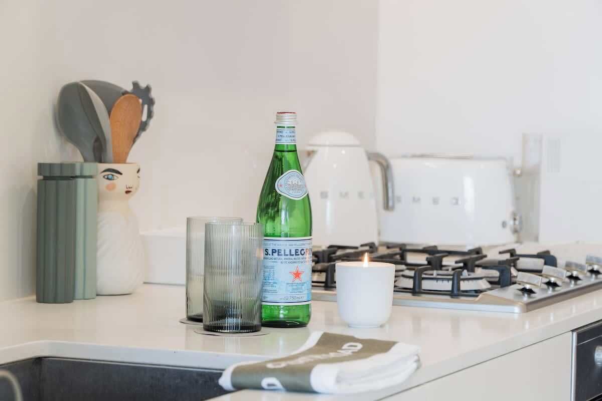 A kitchen counter with a green bottle, a glass, a white mug, and a gas stove.