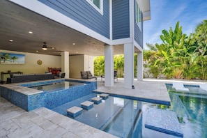 A modern outdoor swimming pool area with a tiled deck, lounge chairs, and a view of lush greenery. - It's Miller Time (Holmes Beach)