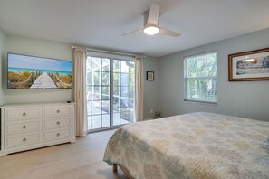 Ein Schlafzimmer mit einem Bett, einem Fernseher, einem Deckenventilator und einem großen Fenster.