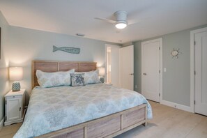 Une chambre à coucher comprenant un lit, des tables de chevet, un ventilateur de plafond et un mur orné d’un décor en forme de poisson.