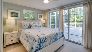 Een slaapkamer met een bed, twee nachtkastjes, een plafondventilator en een groot raam met gordijnen.