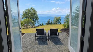 An open sliding glass door leading to an outdoor seating area with two chairs and a view of the ocean.